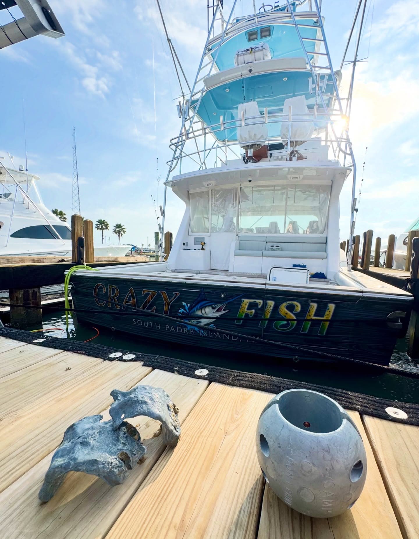 Sportfishing boat Crazy Fish docked behind two worn marine anodes displayed on the pier.
