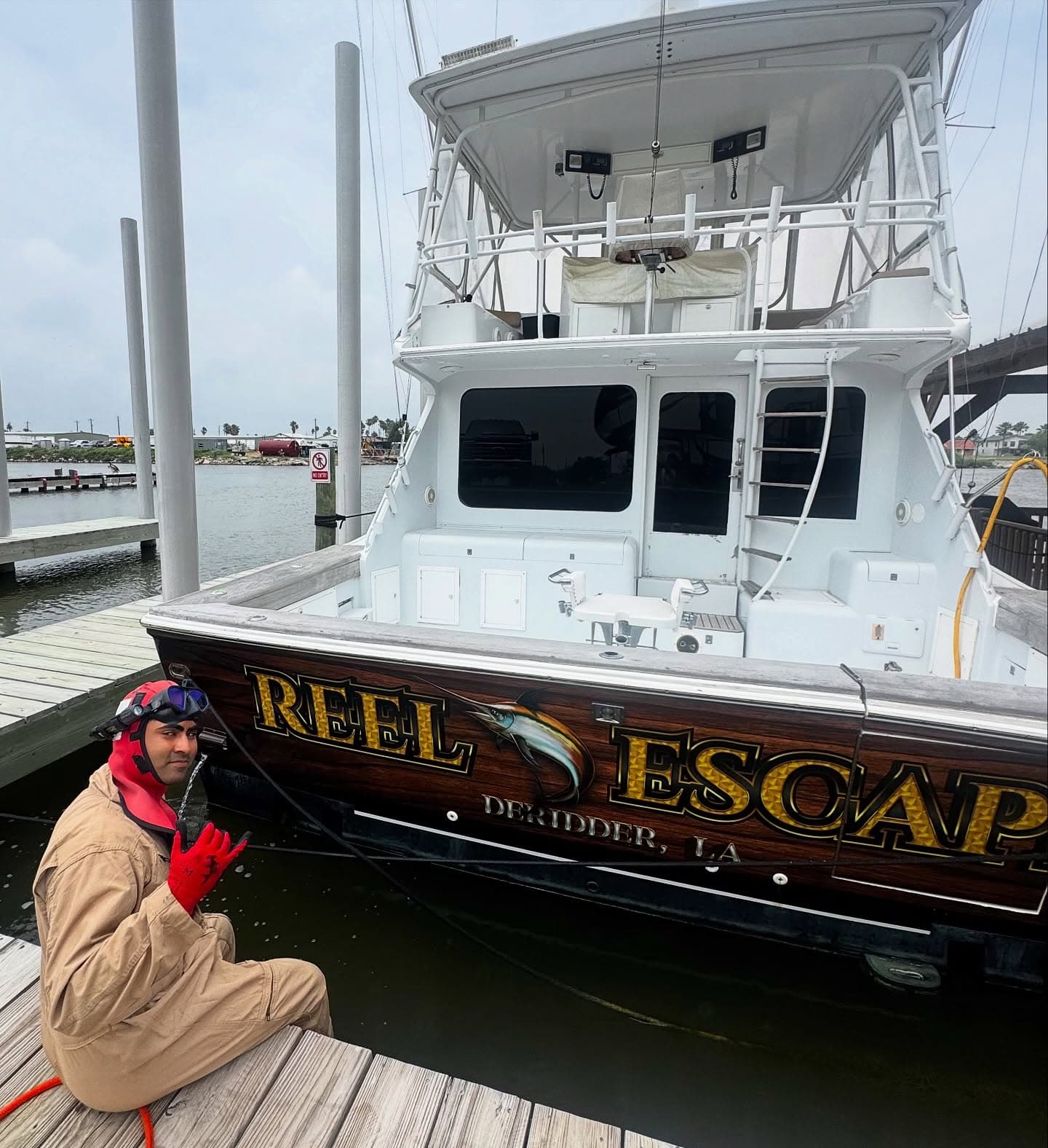 An SPI Dive Services diver kneels on a dock beside the sportfishing boat Reel Escape.