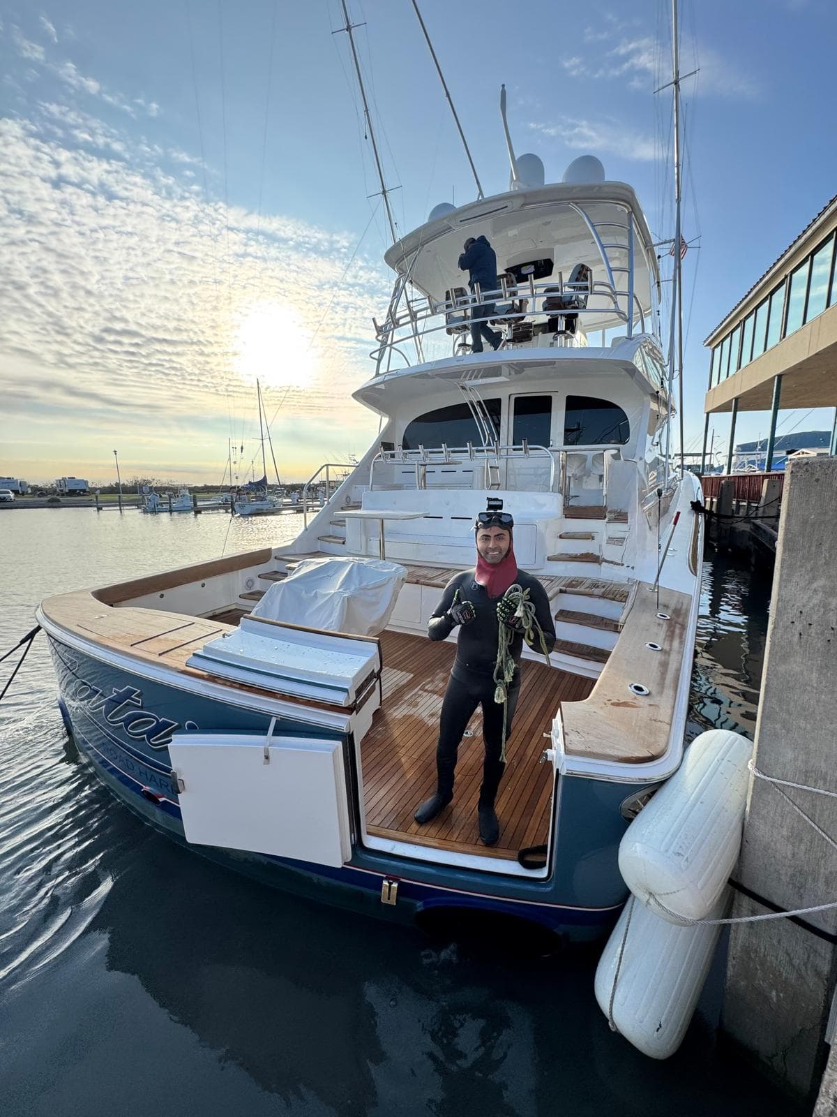 An SPI Dive Services diver stands on the stern of a yacht docked at a marina.